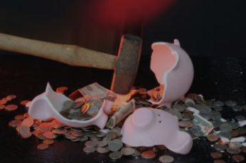 Pink piggy bank being broken by a hammer with coins